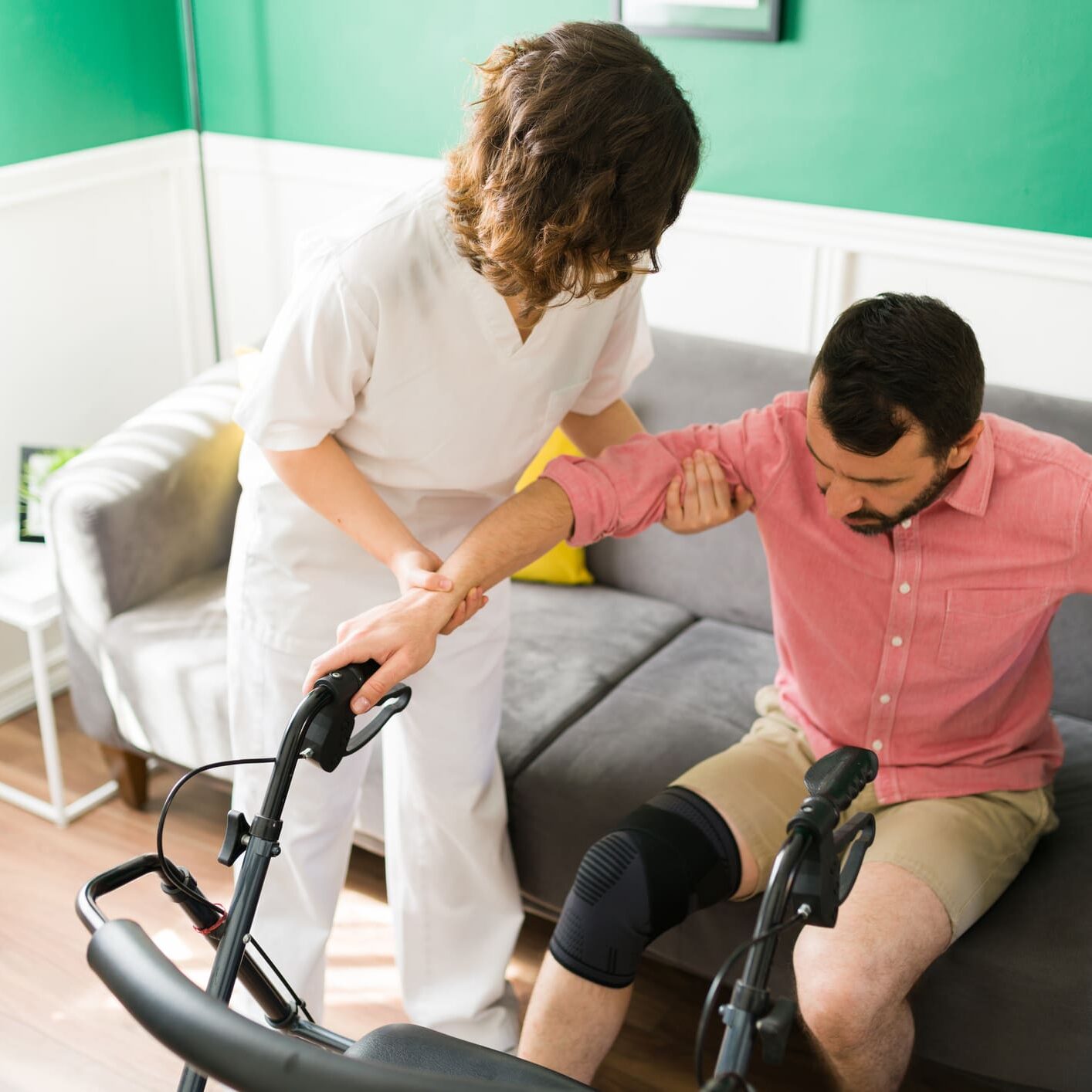Rehabilitation session. Disabled man with a knee injury trying to walk with the help of a professional female nurse